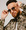 Mann mit Bart und Sonnenbrille blickt in die Kamera. Er trägt eine Jacke mit pixelartigem Muster und hält die Brille mit beiden Händen.