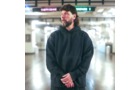 Download Foto: Ein Mann mit Bart steht in einem dunklen Hoodie in einer U-Bahn-Station. Er schaut zur Seite, im Hintergrund verschwommene Schilder.