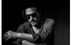 Download Foto: Mann in Schwarz-Weiß, trägt eine Sonnenbrille und ein Hemd, sitzt mit verschränkten Armen, blickt nachdenklich zur Seite.