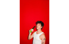 Download Foto: Eine Person in einem weißen Tanktop hält eine Flasche vor einem leuchtend roten Hintergrund.